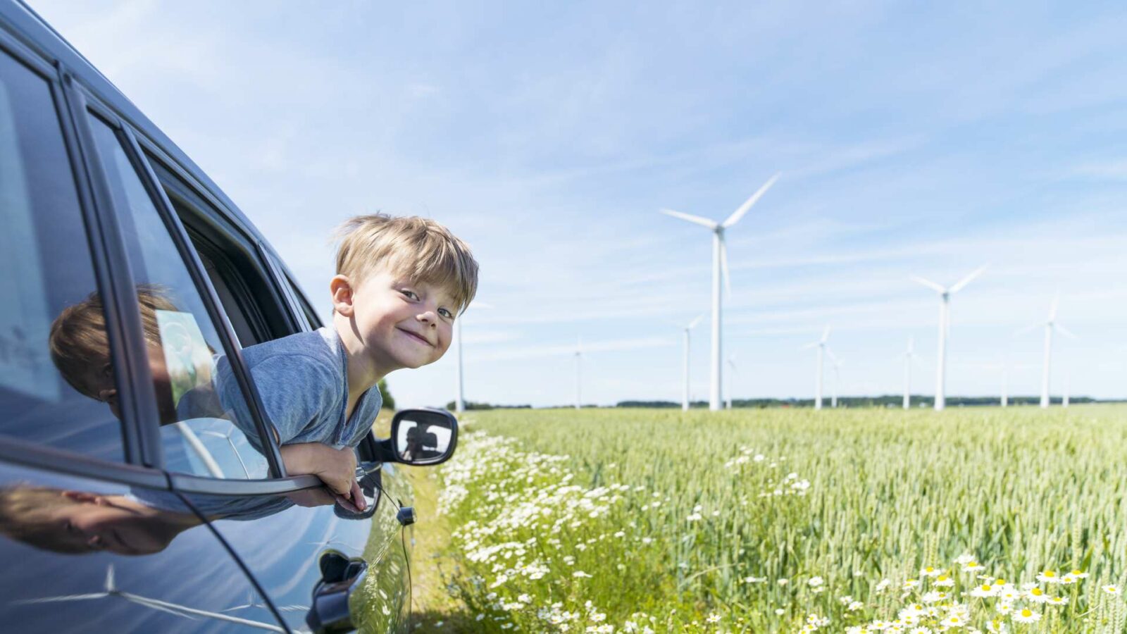 pojke tittar ut igenom ett bilfönster med gröna ängar och vindkraftverk i bakgrunden.