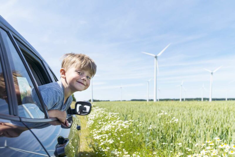 pojke tittar ut igenom ett bilfönster med gröna ängar och vindkraftverk i bakgrunden.