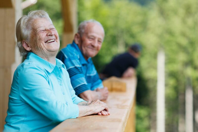äldre kvinna och man lutar sig mot ett räcke och skrattar