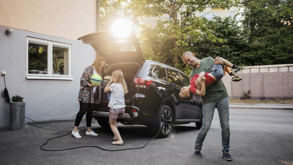 en glad familj packar in saker i en elbil