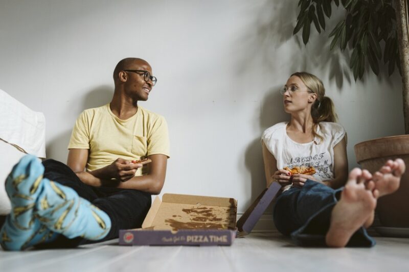 en tjej och en kille sitter på golvet och delar en pizza
