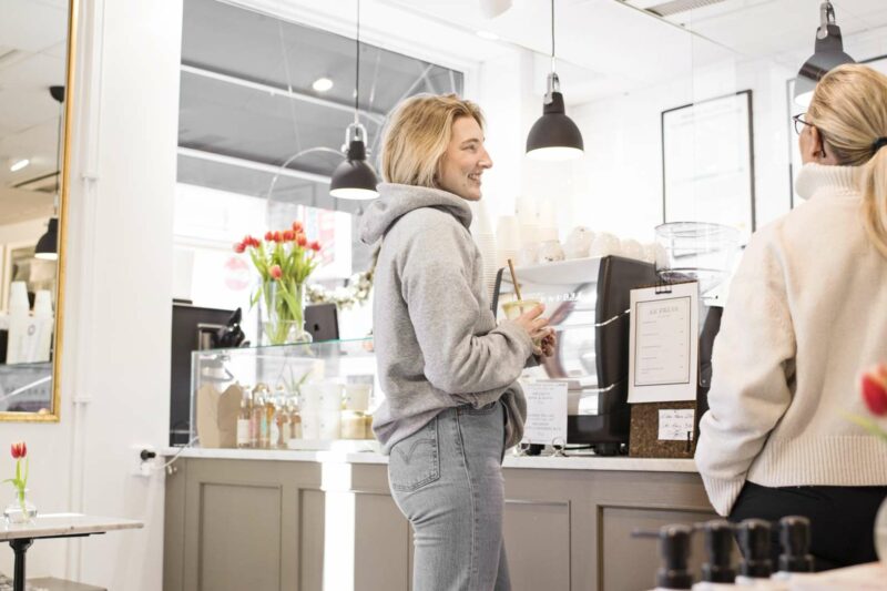 två tjejer ler och beställer kaffe på ett cafe